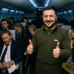 Zelenskyy smiles with two thumbs up on a plane while weary European diplomats slump in coach seats behind him.