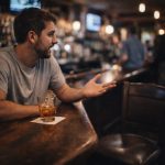 Man alone at bar with drink and empty chair